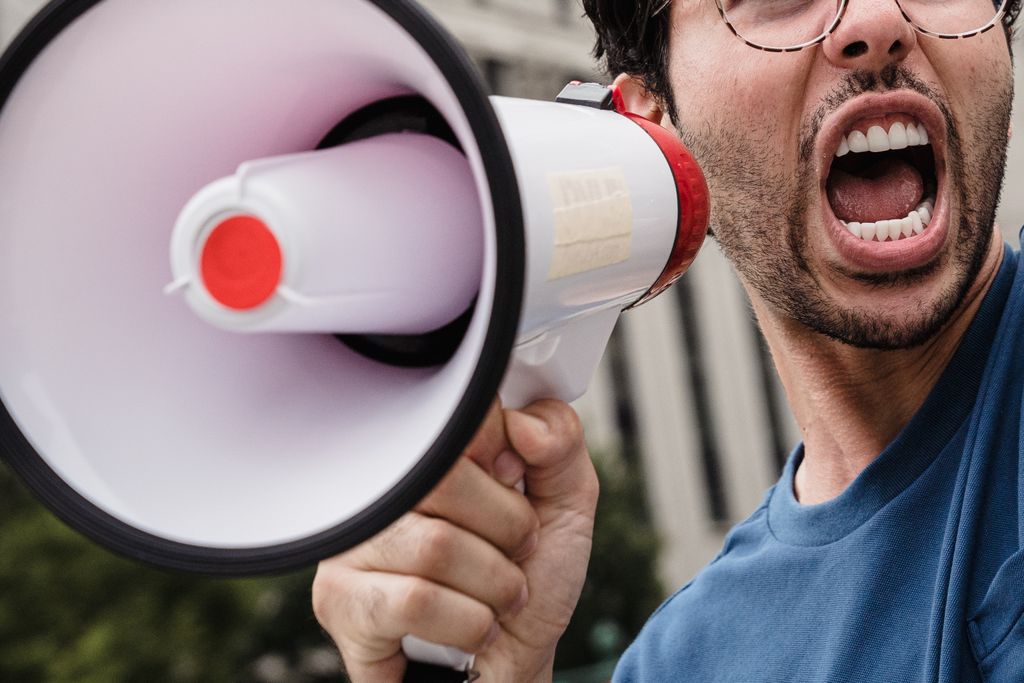 Close-up of a man passionately shouting through a megaphone during a protest.